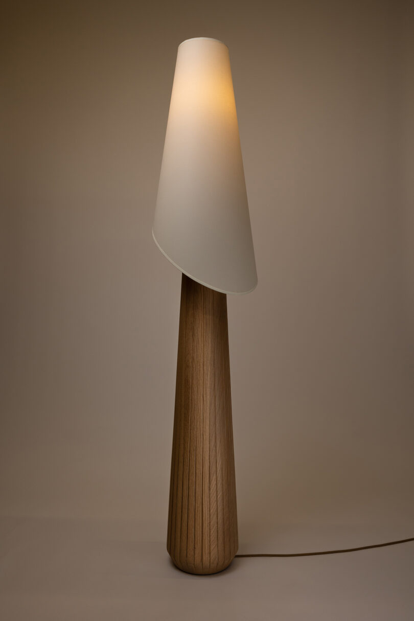 A modern floor lamp with a conical wooden base and a slightly tilted white shade against a plain background.