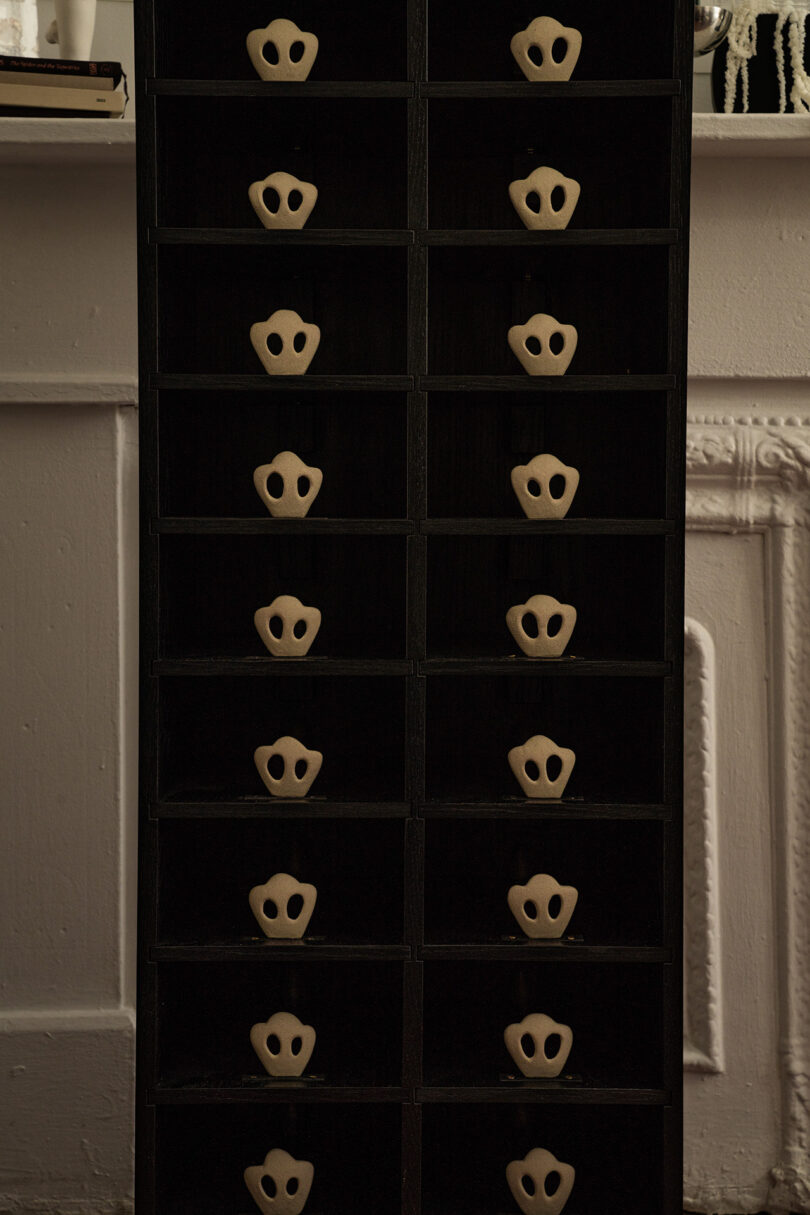 A dark-colored, multi-drawer storage unit with handles shaped like faces, standing in front of a white fireplace.