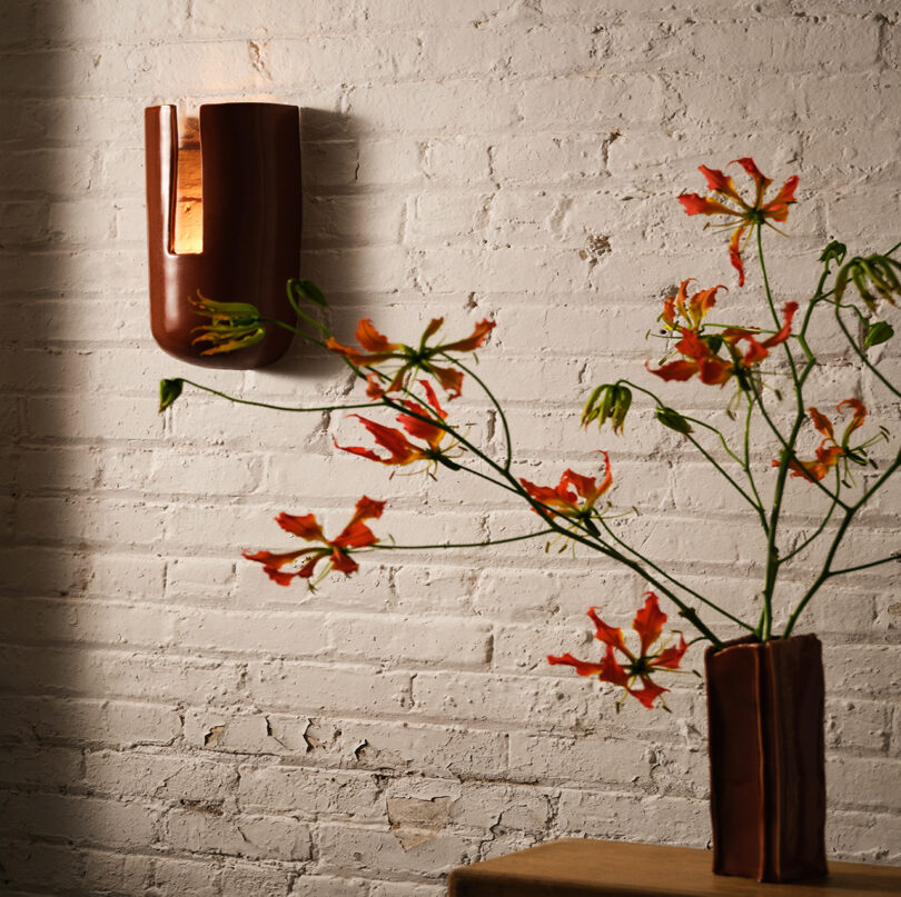 A minimalist wall sconce and vase with orange flowers against a white brick wall.