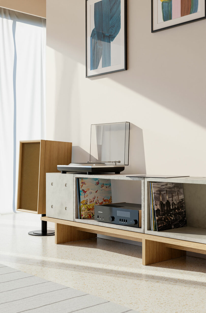 A modern living room features a vinyl record player, amplifier, and a collection of records on a wooden shelf. Two framed artworks hang on the wall above.