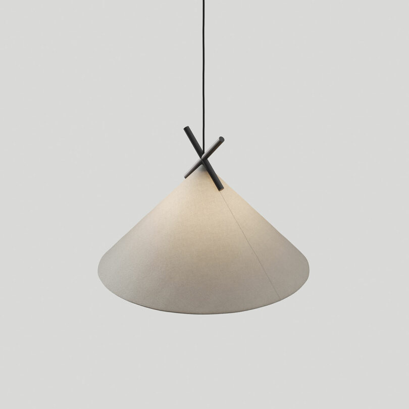 A cone-shaped hanging pendant light with a minimalist design, featuring a beige lampshade and a black X-shaped support structure.