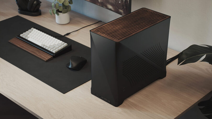 Dark walnut wood slat covers the top of a black case PC gaming rig set across a modern light wood topped desk, with wired mechanical keyboard and mouse nearby.