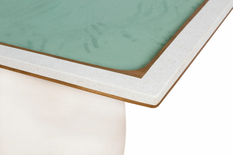 Close-up of a table corner, featuring a green frosted glass top with a white and wooden border, and a white cylindrical base designed by James de Wulf.