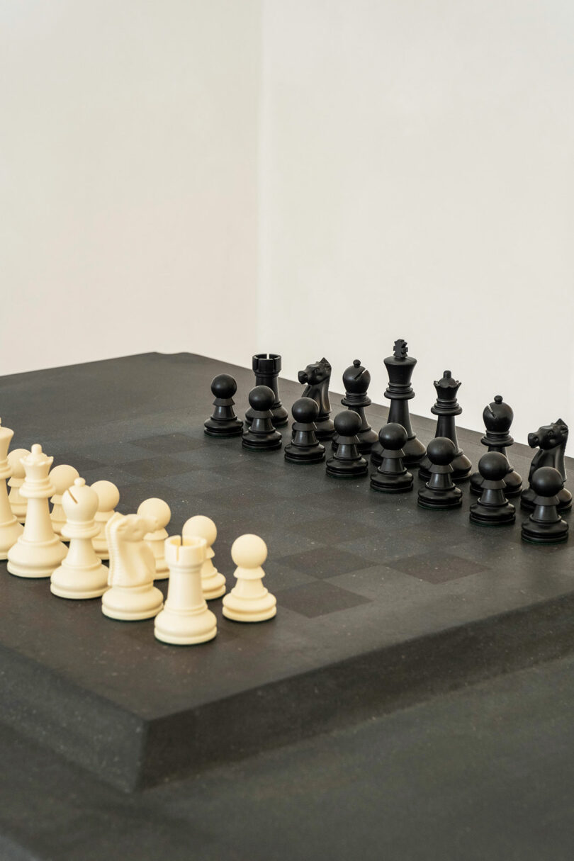 A chessboard with black and white chess pieces, designed by James de Wulf, set up for a game. The white pieces are on the left side and the black pieces on the right side.