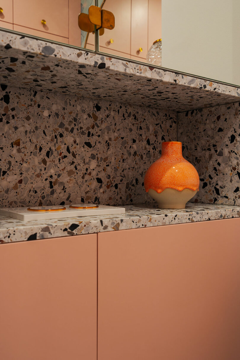 A kitchen countertop with a terrazzo surface, beige cabinets, and an orange vase.