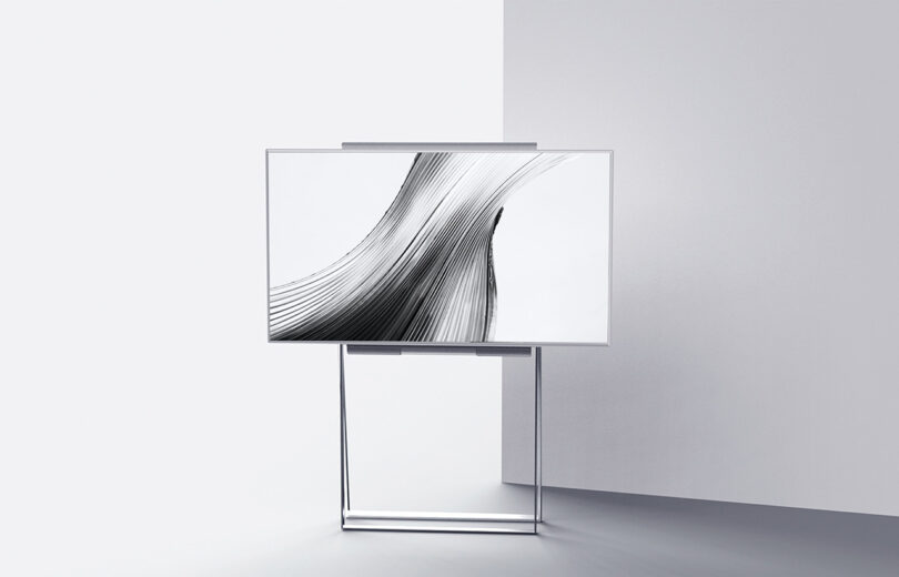 Modern flat-screen LG FLOW concept television displaying abstract black and white art on a stand in a minimalist, white room.