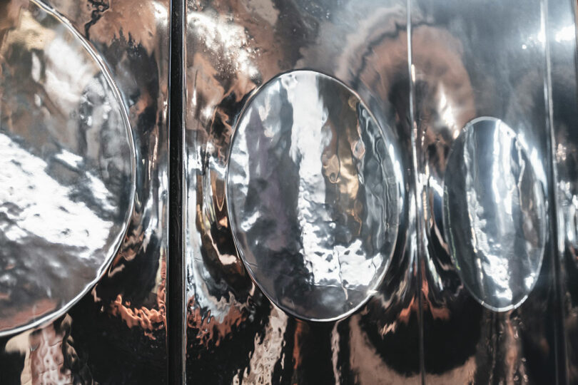 Close-up of a reflective metallic surface featuring several circular, concave indentations, giving the appearance of distorted reflections.