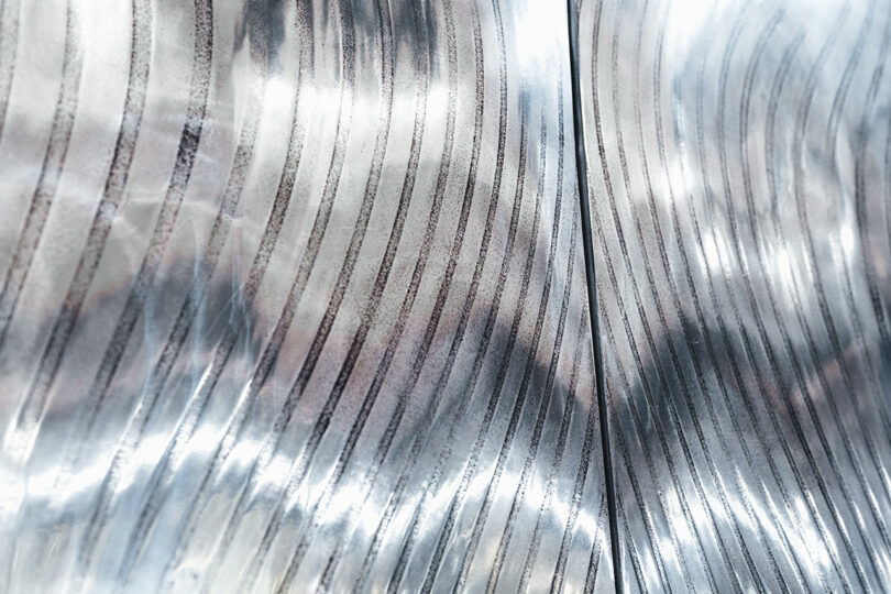 Close-up of a metallic surface with curved, parallel grooves creating a reflective and textured pattern.