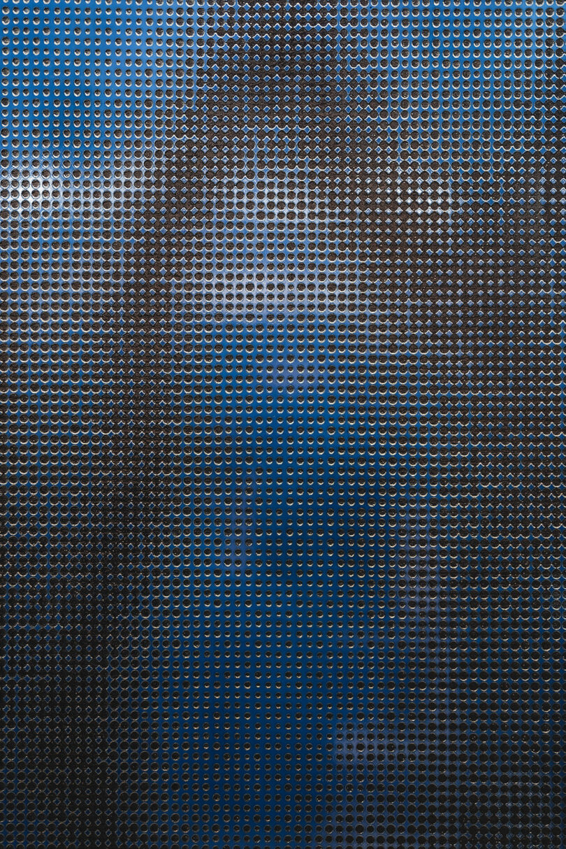 A close-up of a metallic perforated surface with a pattern of evenly spaced circular holes, creating a textured and reflective effect. Light and shadows play across the surface, adding depth.
