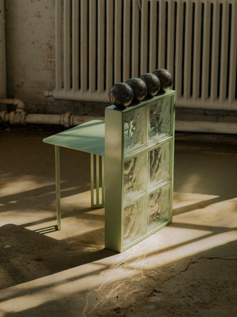 A unique chair with a green frame and glass block backrest, topped with four round black objects.