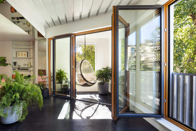 Bright room with large glass doors opening to a patio, featuring indoor plants and a hanging wicker chair.