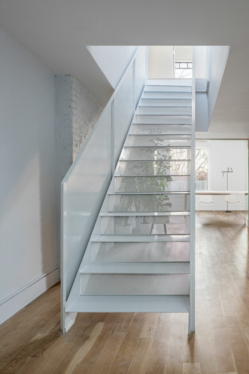 A modern, interior staircase with translucent steps and white railing leading to an upper floor, surrounded by white walls and light wood flooring.