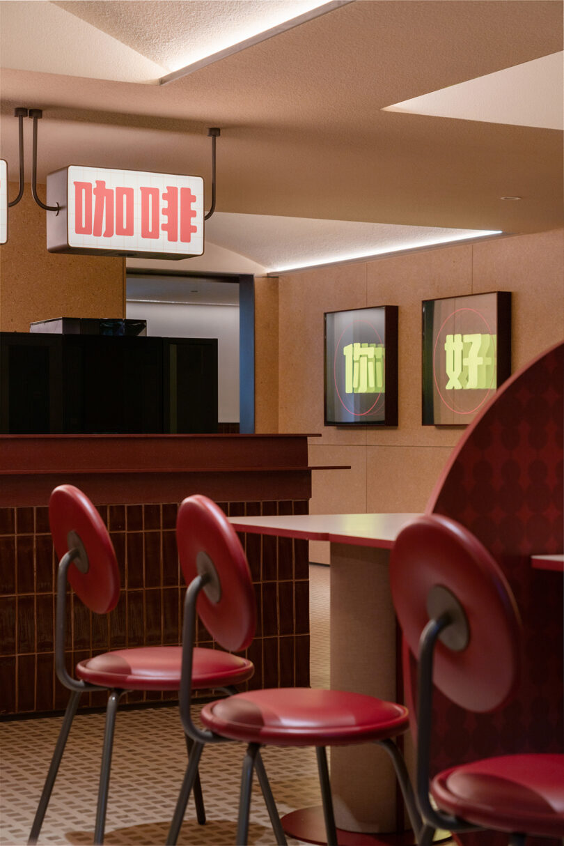 A modern, retro-themed diner with red chairs, a counter, and illuminated signs with Chinese characters hanging from the ceiling. Located within the trendy NI HAO Hotel, the lighting creates a cozy atmosphere.