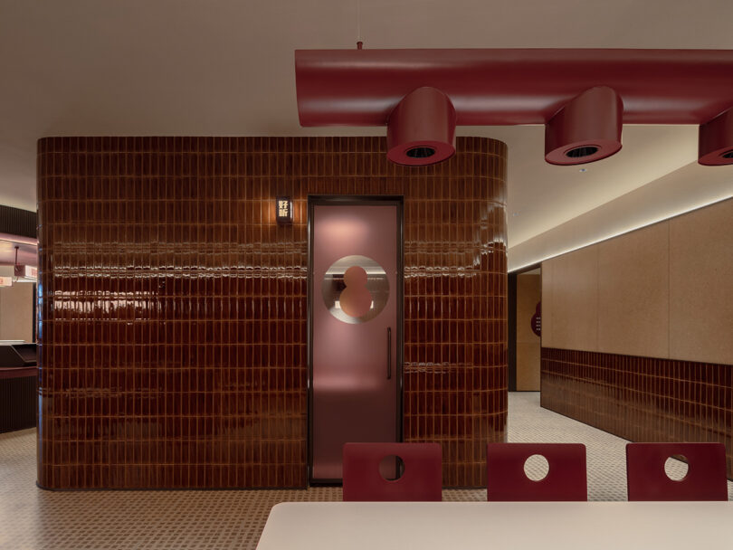 A modern interior space at the NI HAO hotel features glossy brown tile walls, red circular lighting fixtures, a frosted glass door with a round design, and red chairs with circular cutouts around a light-colored table.