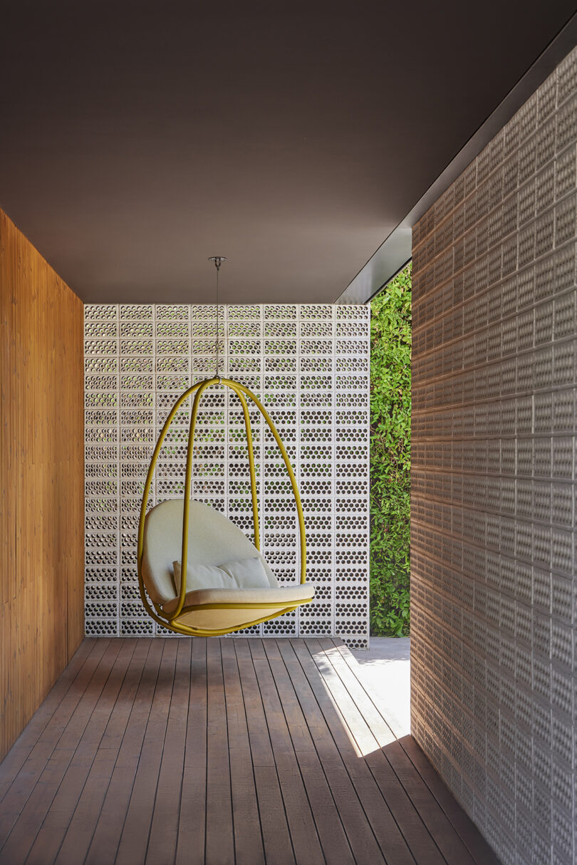 A yellow hanging chair with cushions is placed in a covered outdoor space with a view of greenery outside.
