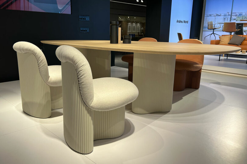 A modern dining table with a wooden top and a set of cushioned chairs featuring ribbed bases, showcased at NeoCon in the Andreu World showroom.