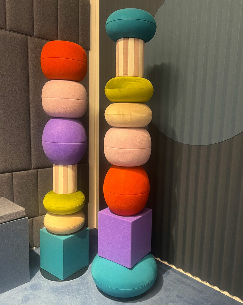 Two colorful, vertically-stacked installations made of cylindrical and round, cushion-like shapes. The left stack has pastel colors while the right stack boasts brighter hues.