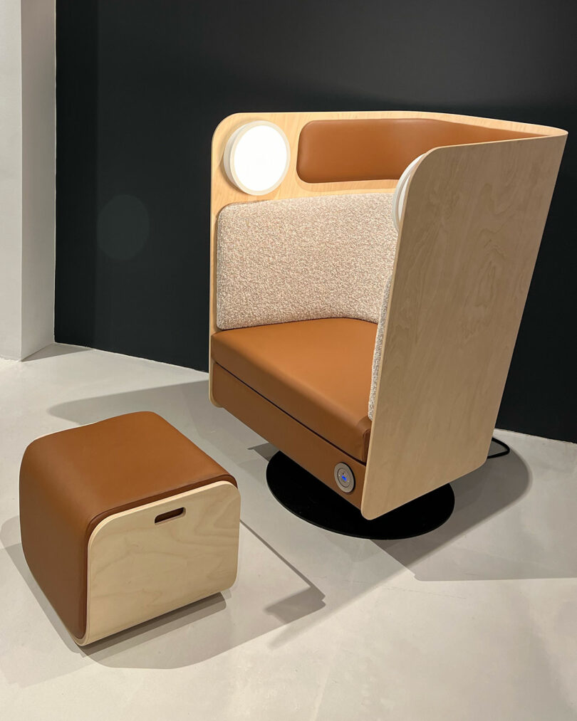 A modern, light wood armchair with a padded backrest and seat, accompanied by a matching ottoman. Both pieces are upholstered in brown and beige fabrics.