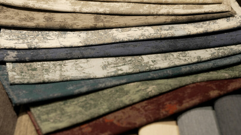 A variety of sustainable fabric swatches in muted, textured colors are laid out in an overlapping arrangement.
