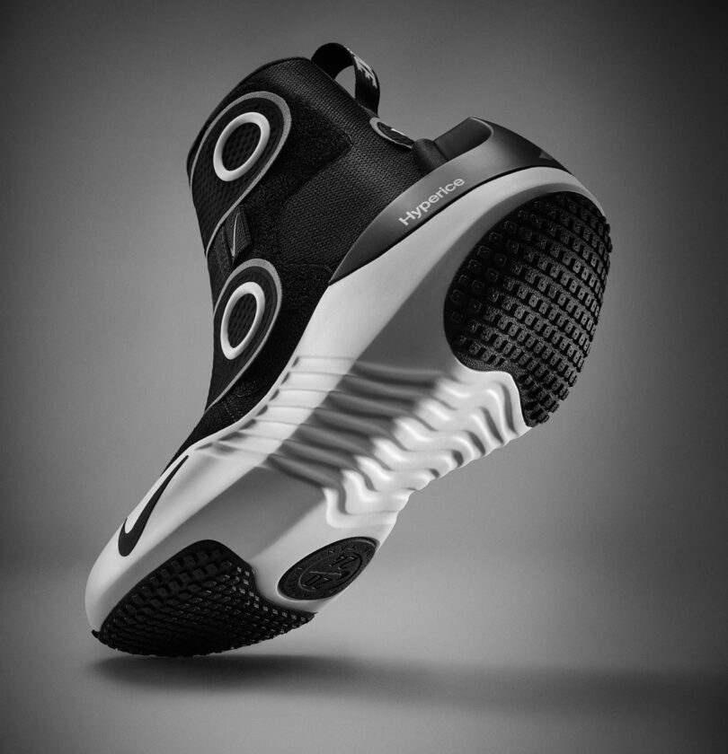 Black and white athletic shoe with circular designs, labeled "Nike x Hyperice," shown against a neutral background. This model incorporates recovery technology for enhanced performance.
