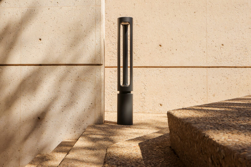Modern outdoor lamp installed near a concrete wall, casting shadows from natural light.