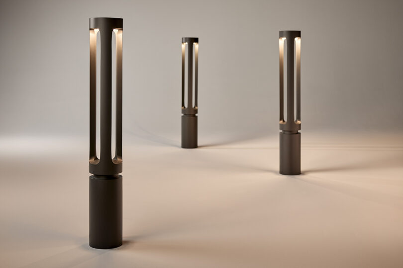 Three modern, cylindrical lamps emit a warm glow in a dimly lit space, creating patterns of light on the floor.