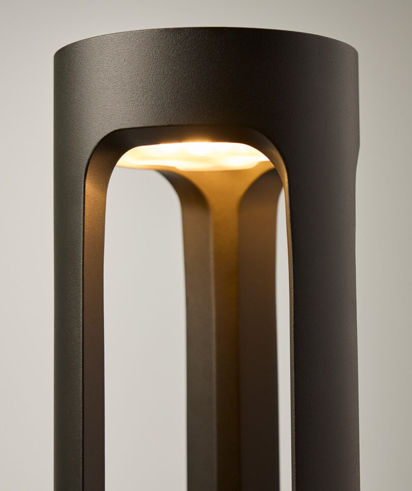 Close-up of a modern black lamp with a cylindrical design, featuring an illuminated light source at the top.