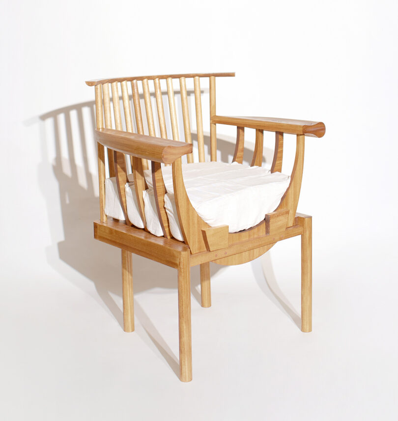A wooden chair with wide armrests and a slatted backrest, featuring a white cushioned seat, set against a plain white background.