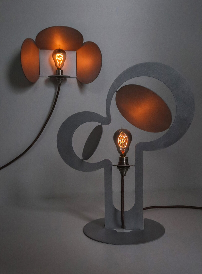 Two artistic light fixtures with exposed filament bulbs. One lamp has a circular design, and the other has overlapping oval shapes. Both emit a warm, soft glow.
