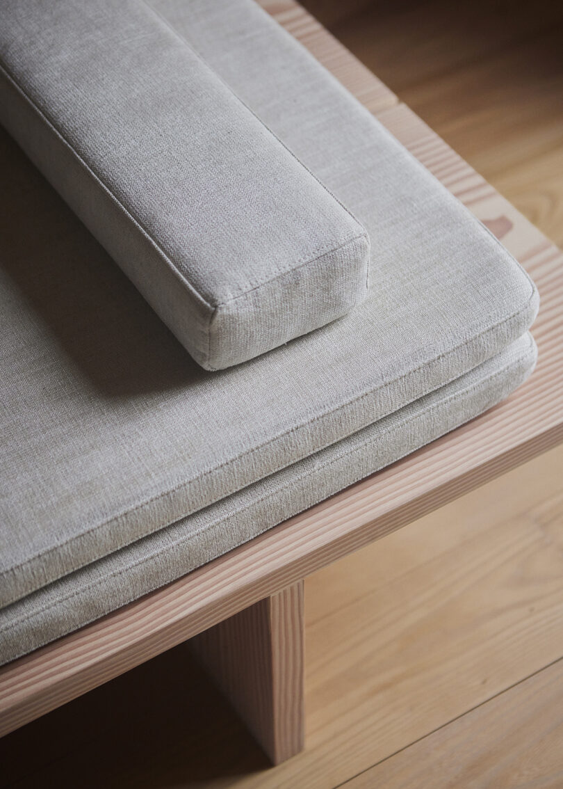 Close-up of a grey upholstered cushion with a rectangular bolster pillow on a light wooden daybed.