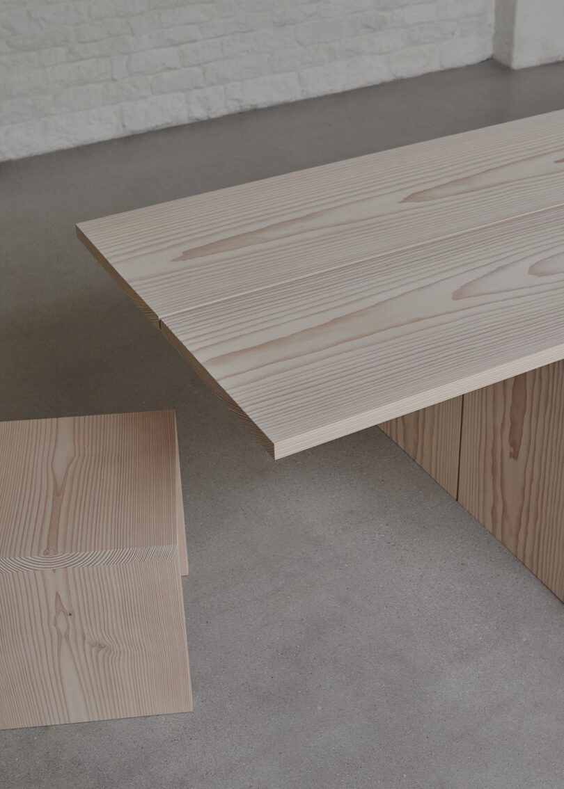 A wooden stool and table with visible wood grain patterns are placed on a smooth, gray floor.