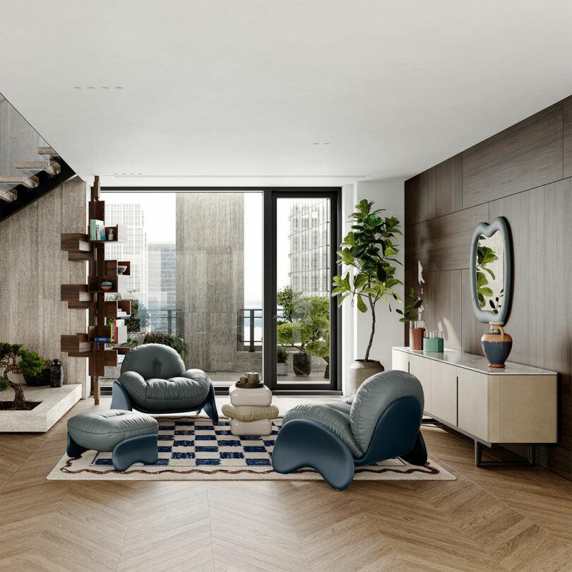 A modern living room with two blue cushioned chairs, matching ottomans, a geometric rug, plants, decorative items, and a bookshelf. Large windows offer a view of city buildings.