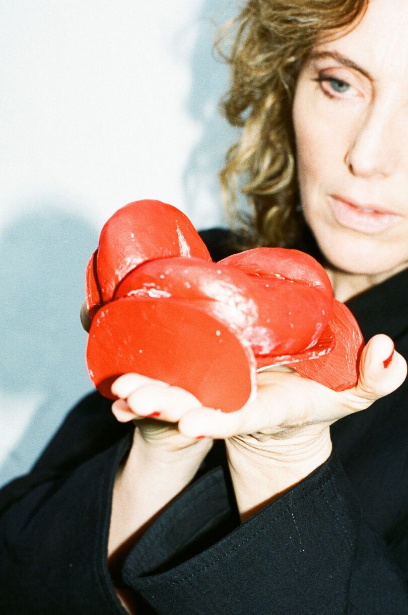 A person with curly hair holds several red, heart-shaped objects in their hand, wearing a black garment.