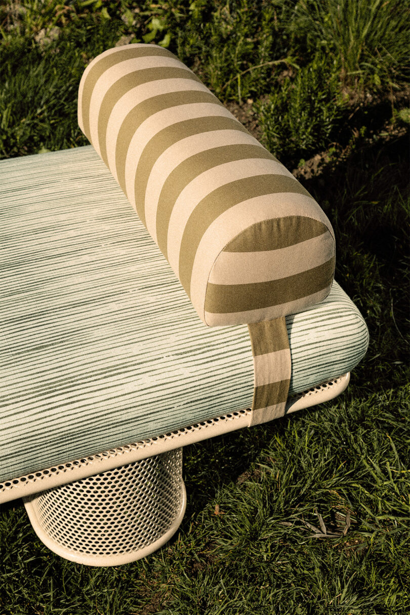 Detail of a bench with a striped cushion is surrounded by lush greenery.
