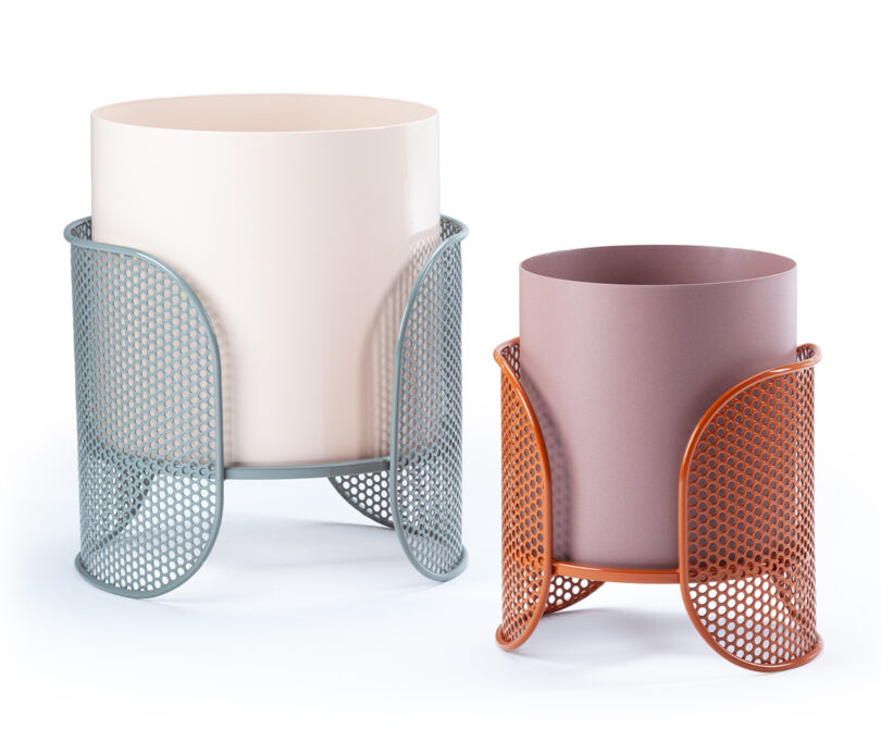 Two cylindrical planters are placed side by side, each within a perforated metal holder. The larger planter is a beige color with a blue holder, and the smaller one is purple with an orange holder.