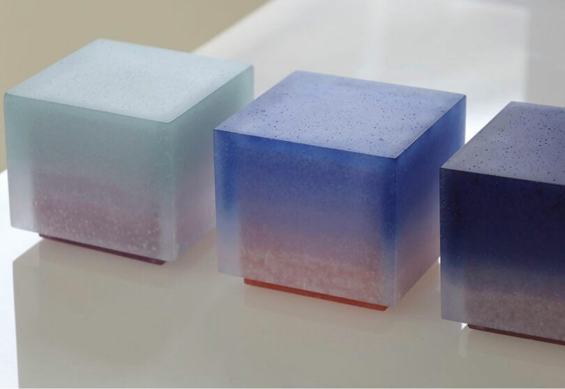 Three gradient-colored translucent cubes with rounded edges, transitioning from light blue at the top to purple and pink at the base, resting on a white reflective surface.