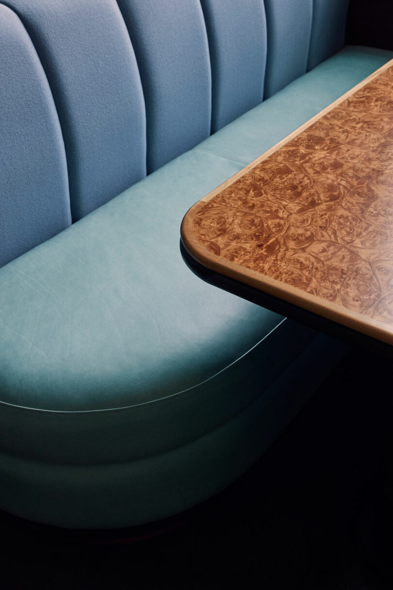 A blue upholstered Malin booth seat next to a brown, wood-textured table.