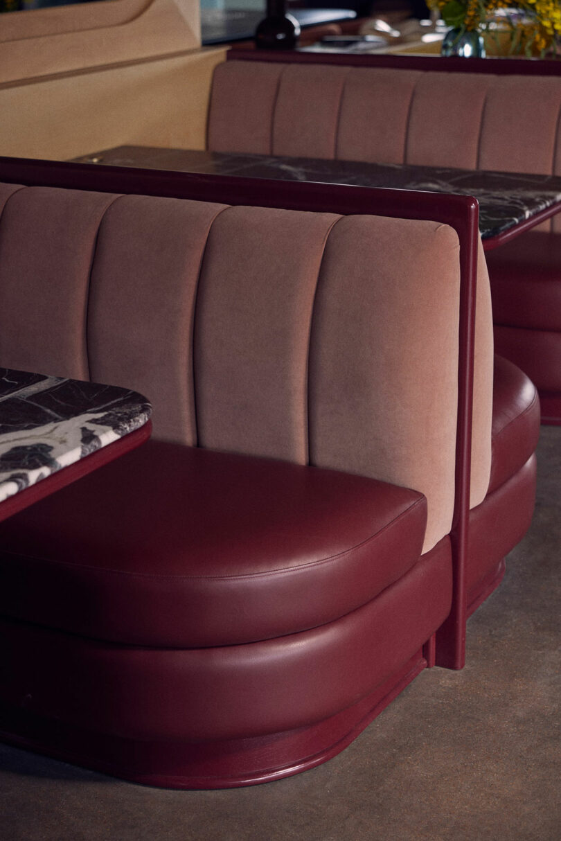 Close-up of restaurant booth seating with maroon leather and beige velvet upholstery. Marble-topped tables are visible in the background.