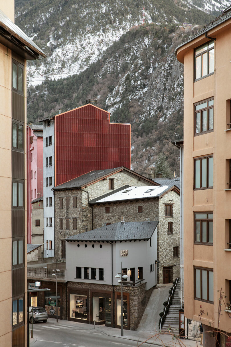 Exterior view of a modern hotel with tall colorful buildings surrounding it with snowy mountains int the background.