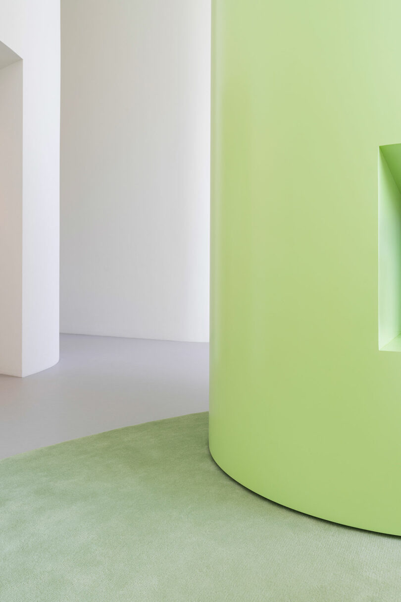 A bright, minimalist corner with a light green cylindrical structure and a soft green carpet against a white wall.