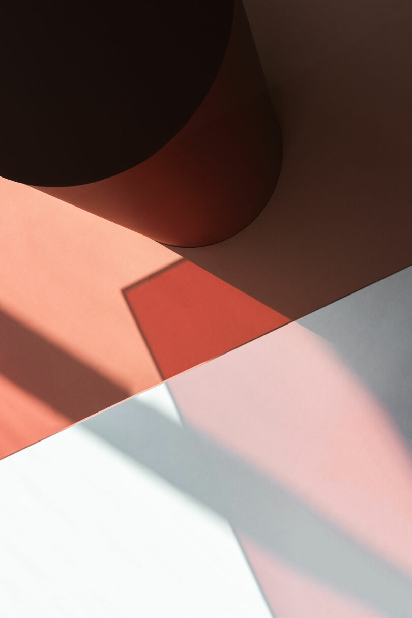 Shadows and light fall on geometric shapes in varying shades of brown, pink, and white, creating a minimalist abstract composition.