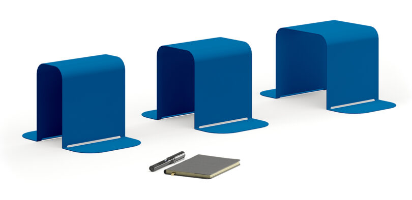 Three blue Fantin bookends positioned upright side by side with a pen and a notebook placed in front of them.