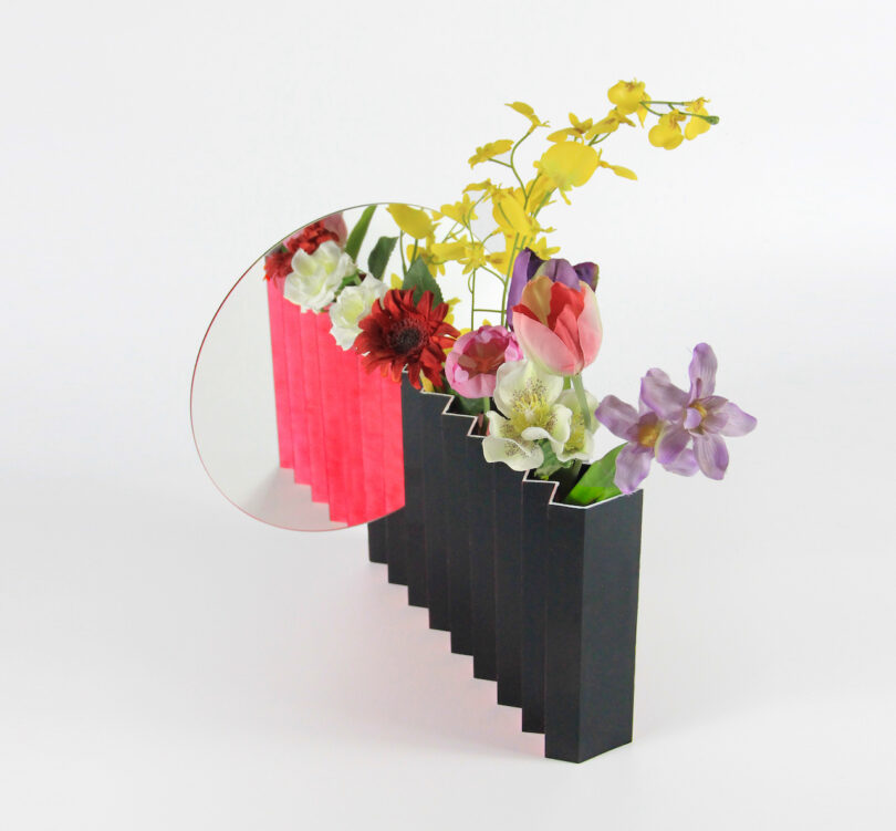 a black vase with a mirror attached and flowers in it