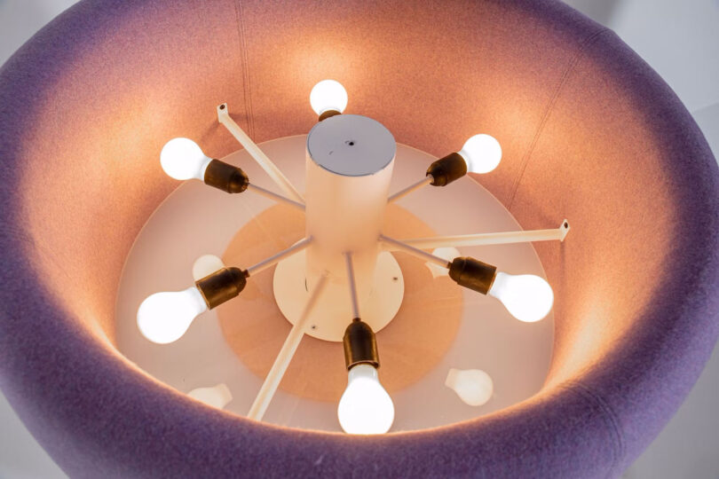 Close-up view of a modern floor lamp fixture featuring multiple exposed lightbulbs arranged in a circular pattern, surrounded by a purple fabric shade