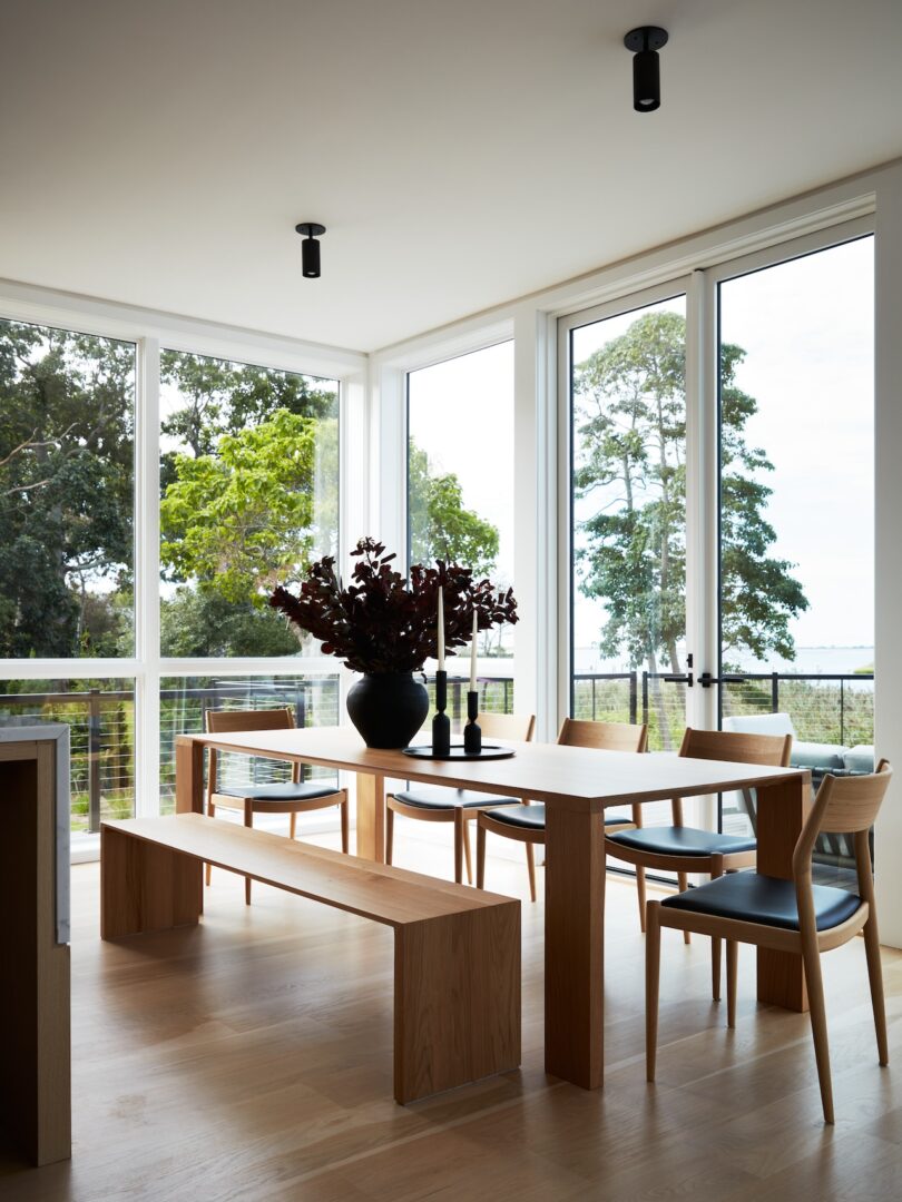 Dining area with wooden table, bench, and chairs, surrounded by large windows
