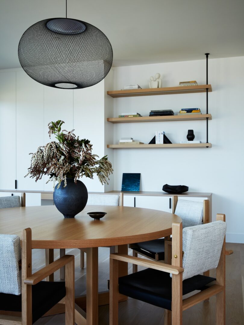 Dining area with round wooden table, upholstered chairs, and a large pendant light