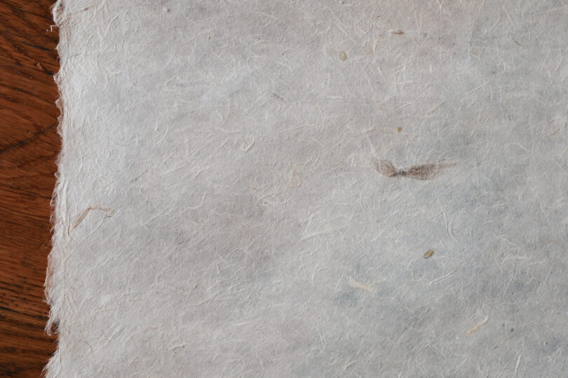 A close-up view of a piece of textured white paper with fibers visible, placed on a wooden surface