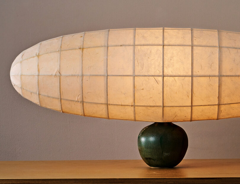 A lit, rounded paper lamp is mounted on top of a small green ceramic base, placed on a wooden surface.