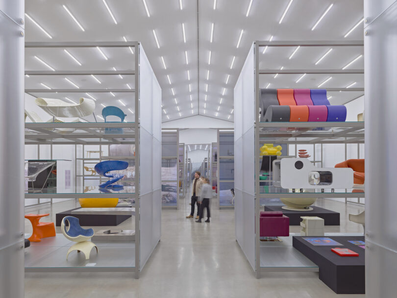 Two people in a modern, well-lit gallery featuring futuristic designs displayed on shelves and pedestals.