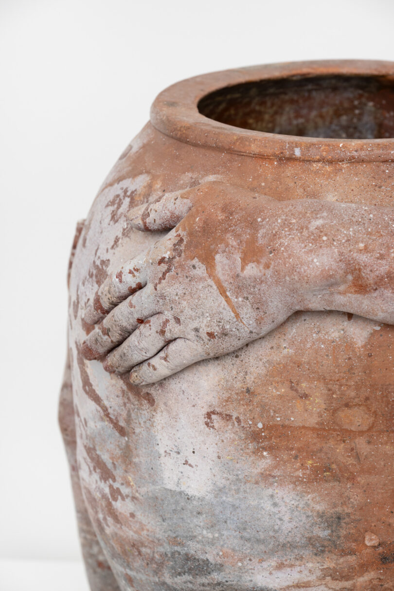 Sculpture of hand rests on side of clay vessel.